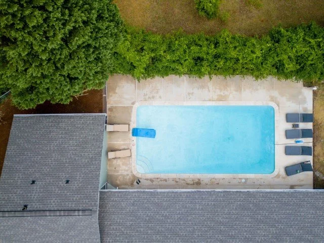 A backyard pool area with a pool, lounge chairs, and surrounding greenery.