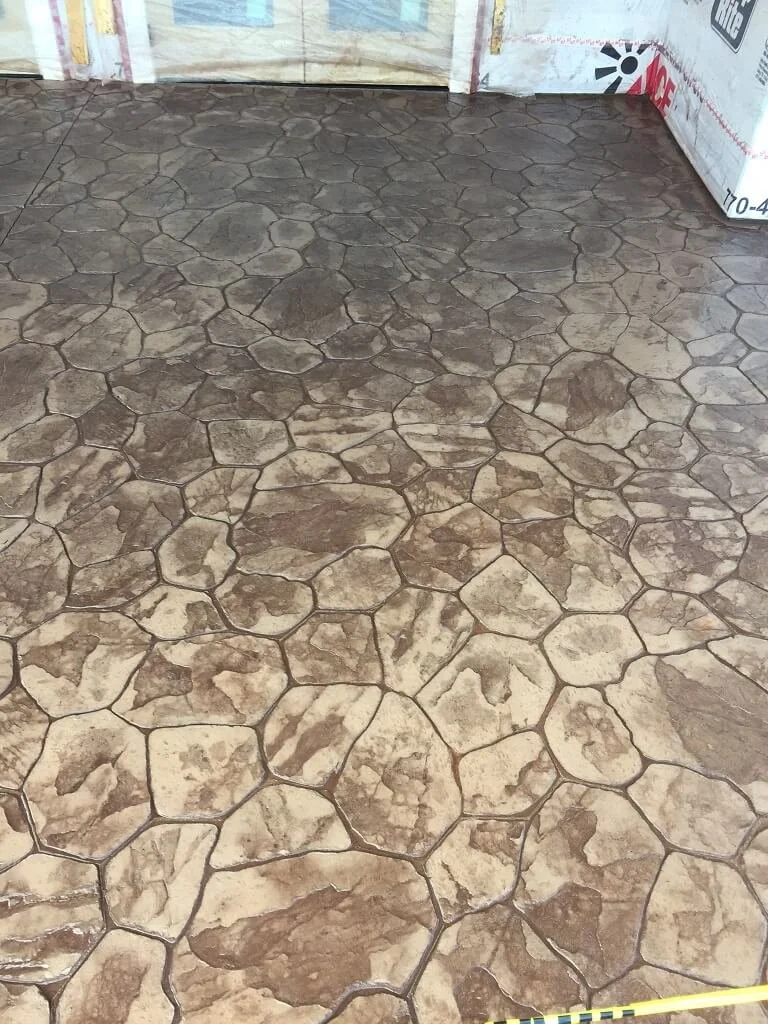 Concrete floor with a stamped pattern resembling irregular stones in shades of brown and tan, with visible cracks.