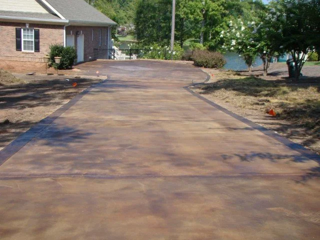New concrete driveway leading to a house with trees and shrubs on the sides.
