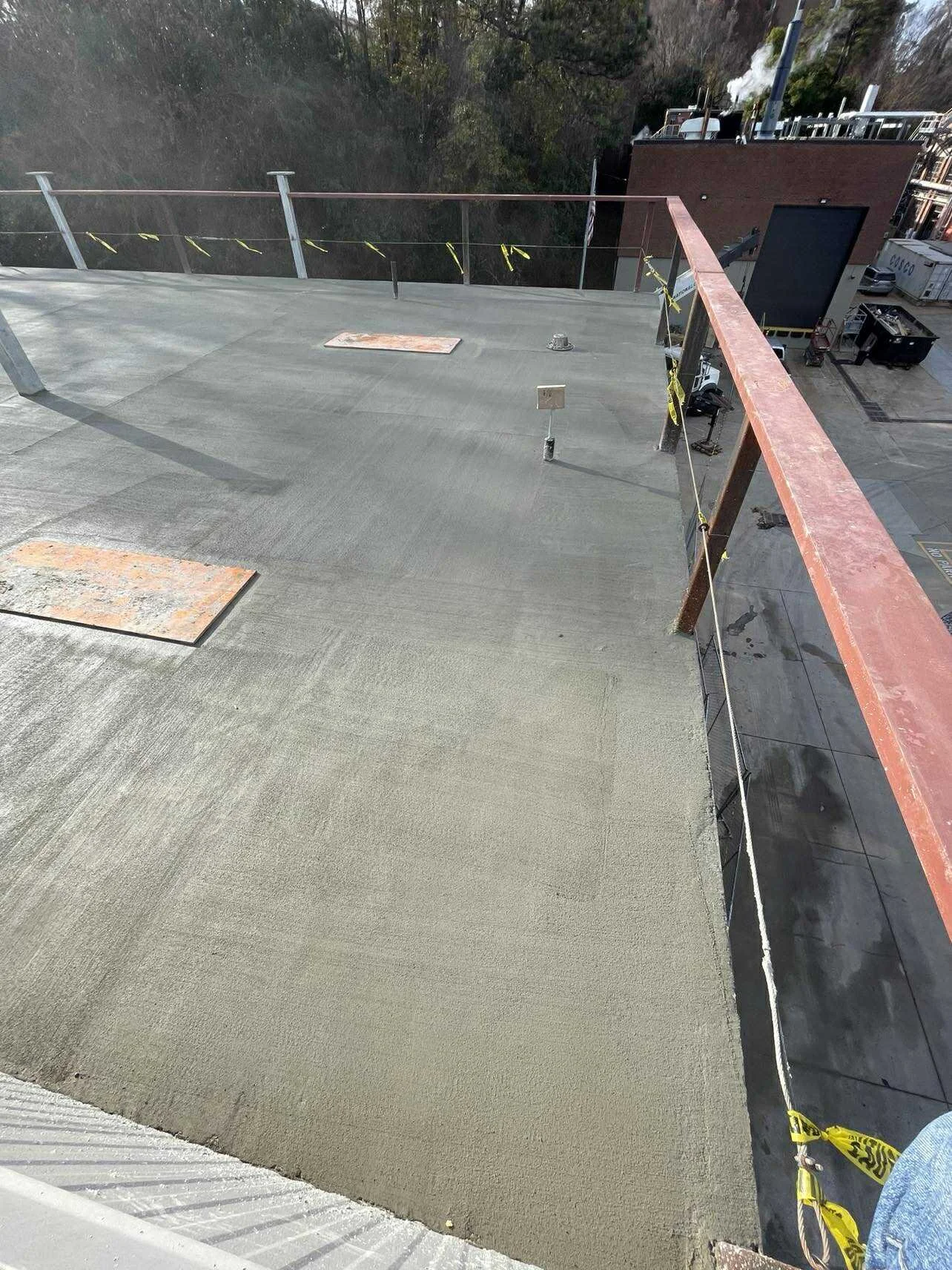 Newly poured concrete on a rooftop with safety railing, construction materials, and equipment.