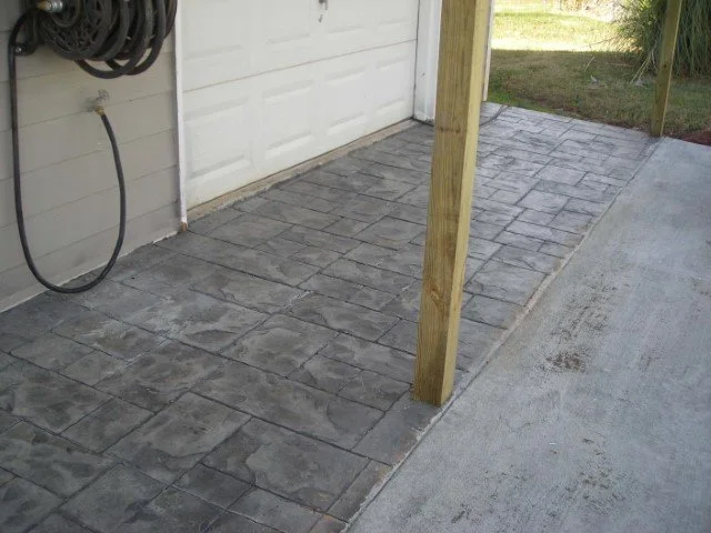 Concrete pavers being installed next to a garage and a wooden post.