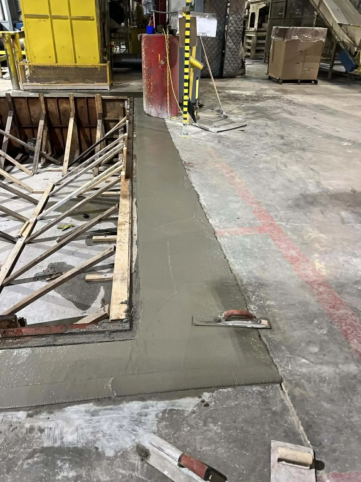 Construction site with concrete pouring for sidewalk, wood framing, and various tools and equipment visible.