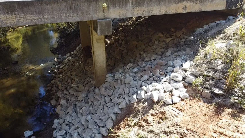 Support beams of a bridge resting on a pile of rocks underneath.