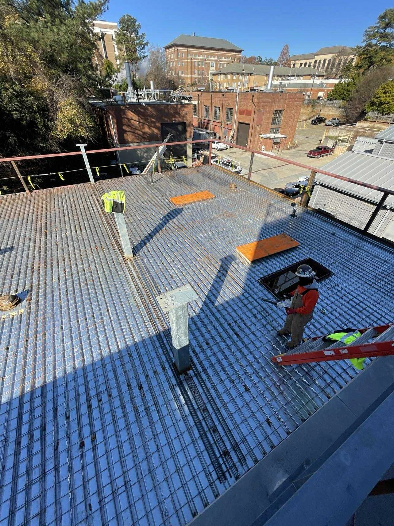 Workers on a rooftop installing solar panels or reflective roofing material, with buildings and trees in the background.