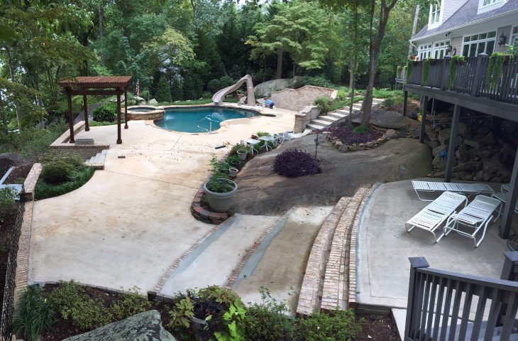 Backyard with a small pool, slide, shaded area, lawn chairs, raised deck, and landscaped garden.