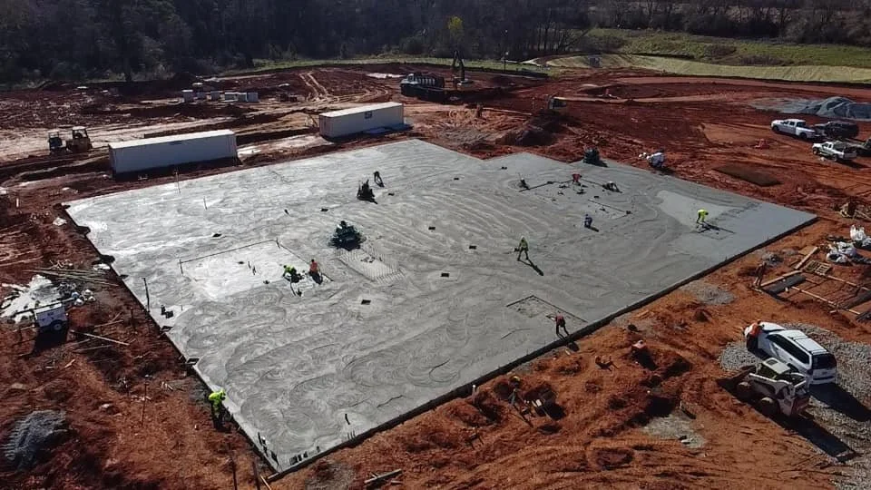Construction workers pouring concrete on a foundation for a building at a construction site, surrounded by vehicles and equipment.