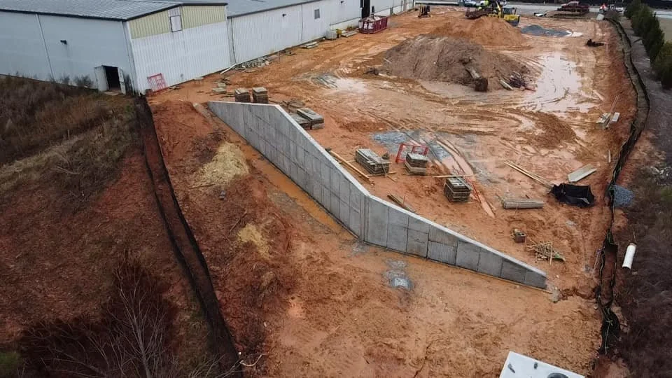 Construction site with a retaining wall built on a dirt slope, with construction materials and equipment scattered around.
