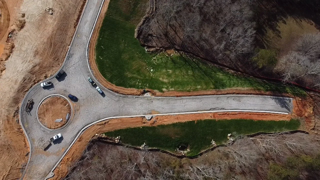 Aerial view of a newly constructed cul-de-sac with cars parked around it, surrounded by grass and trees with some areas of exposed soil.
