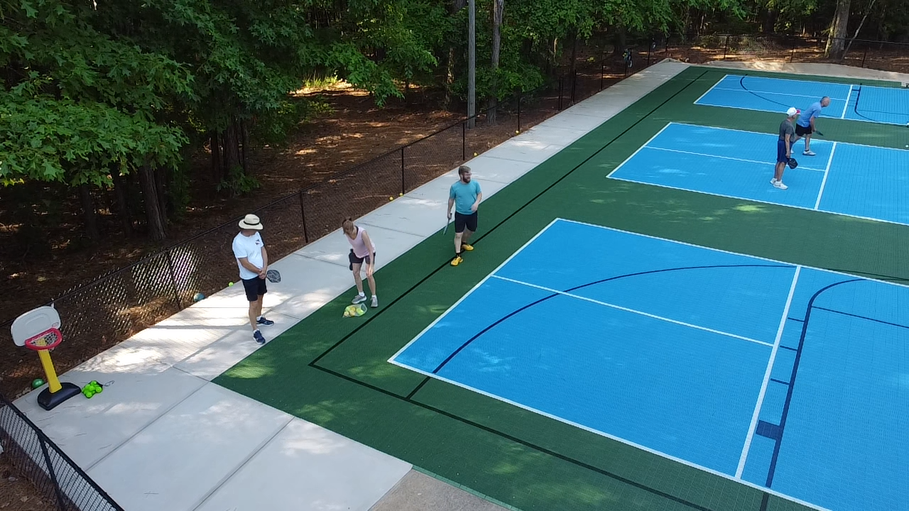 People practicing tennis on outdoor courts surrounded by trees.