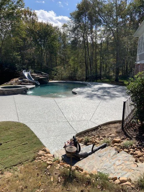 Backyard with in-ground swimming pool, water slide, and surrounding trees.
