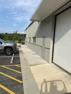 Image of an industrial building with a closed roll-up door, parked cars, and a sidewalk with yellow striped parking lines.
