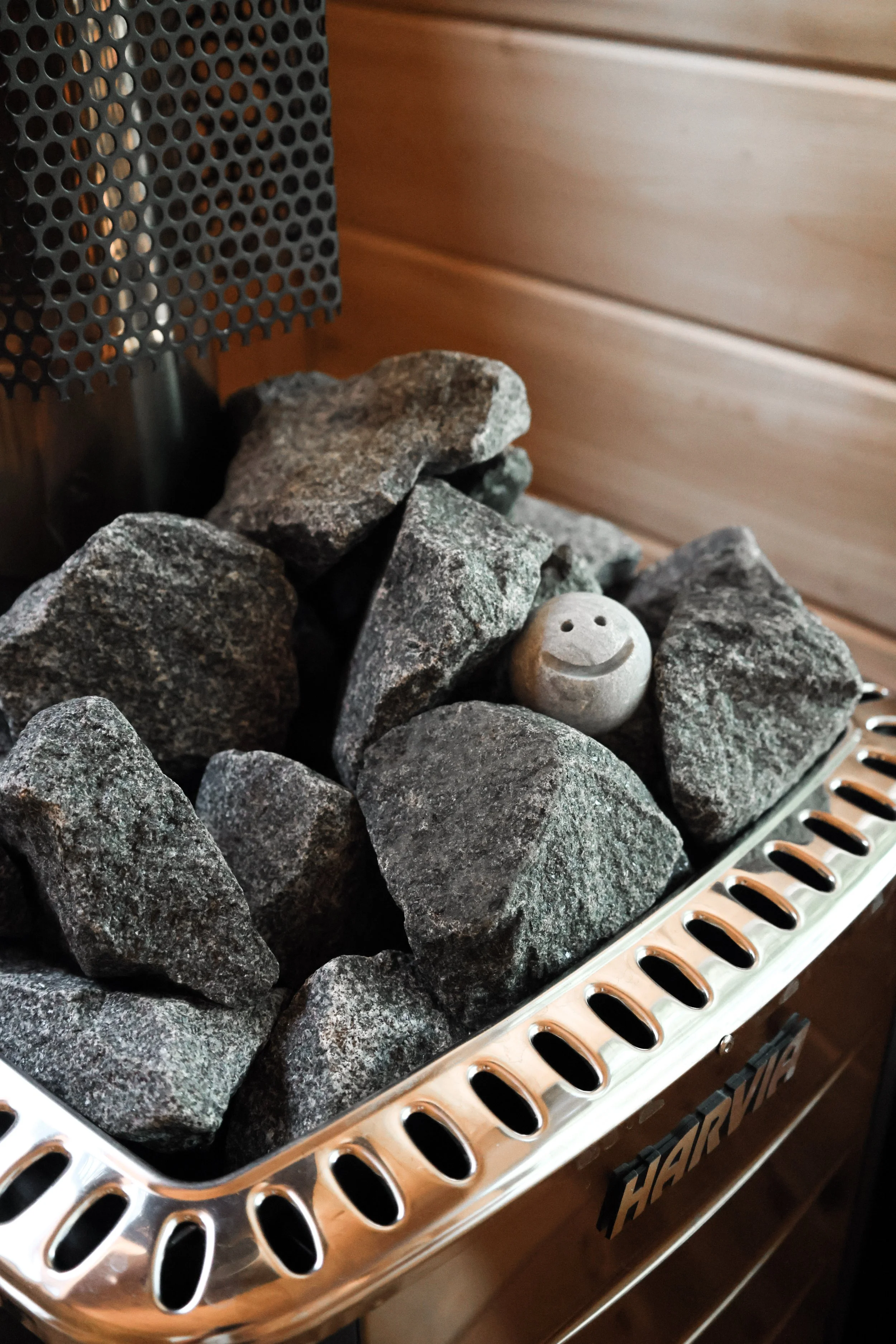 Close-up of sauna stones and a small smiling sauna stone on a traditional Harvia M3 sauna heater.