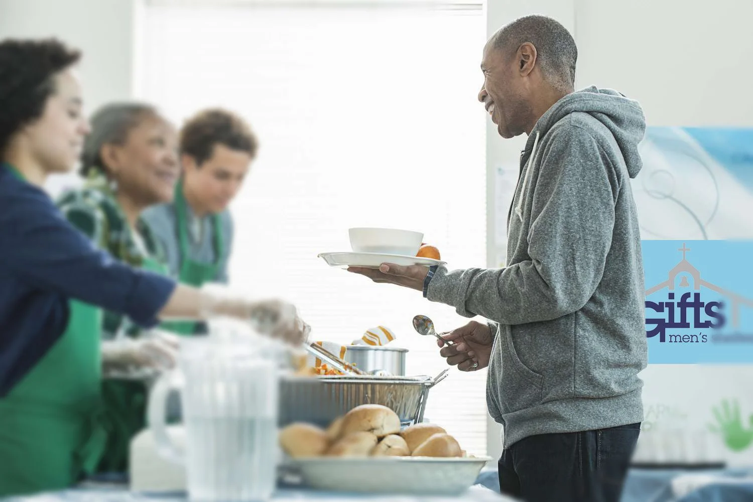 Man receiving food tray from volunteers at a community kitchen or food bank.