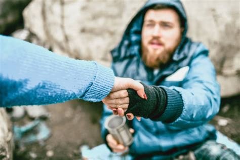 Two people exchanging a coin in an outdoor setting with rocky background, one person wearing a blue jacket and gloves, the other extending a hand with a coin.