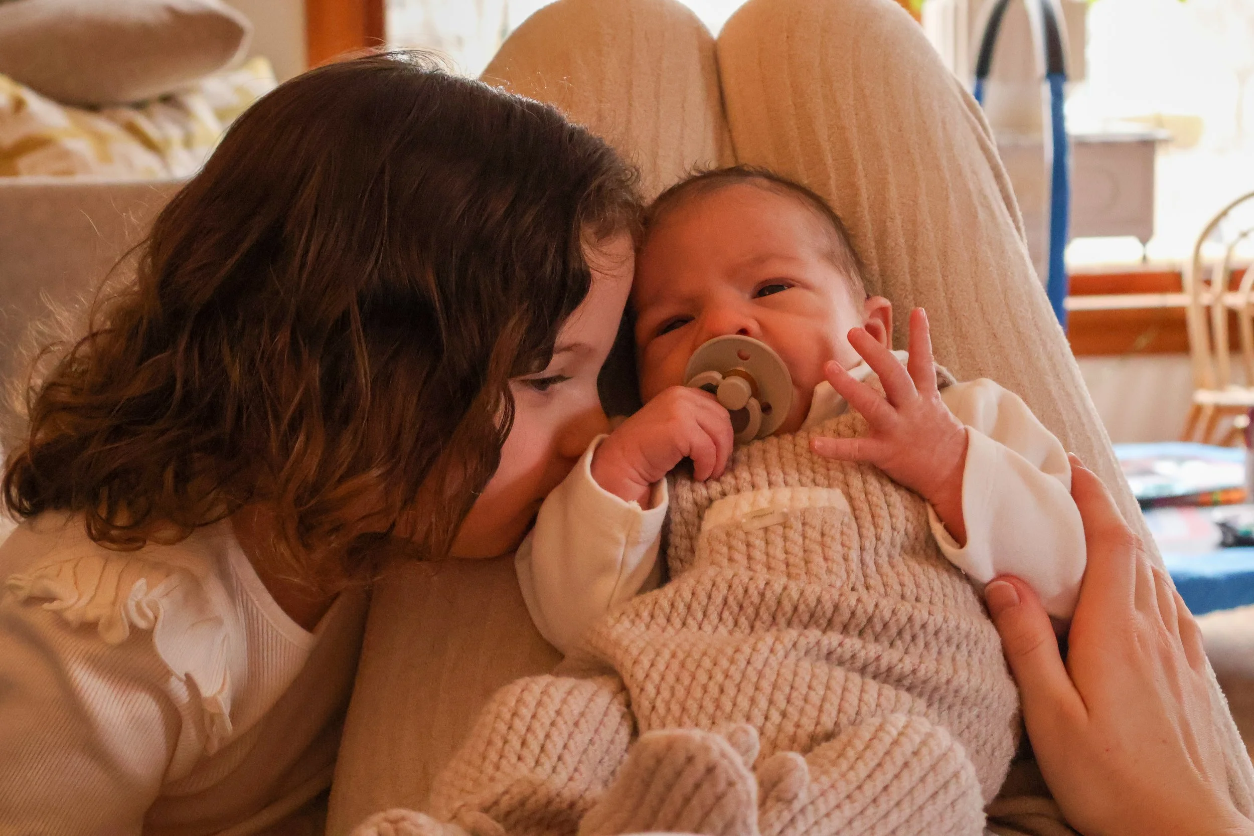 A woman holding a baby with a pacifier, both close to each other, indoors.