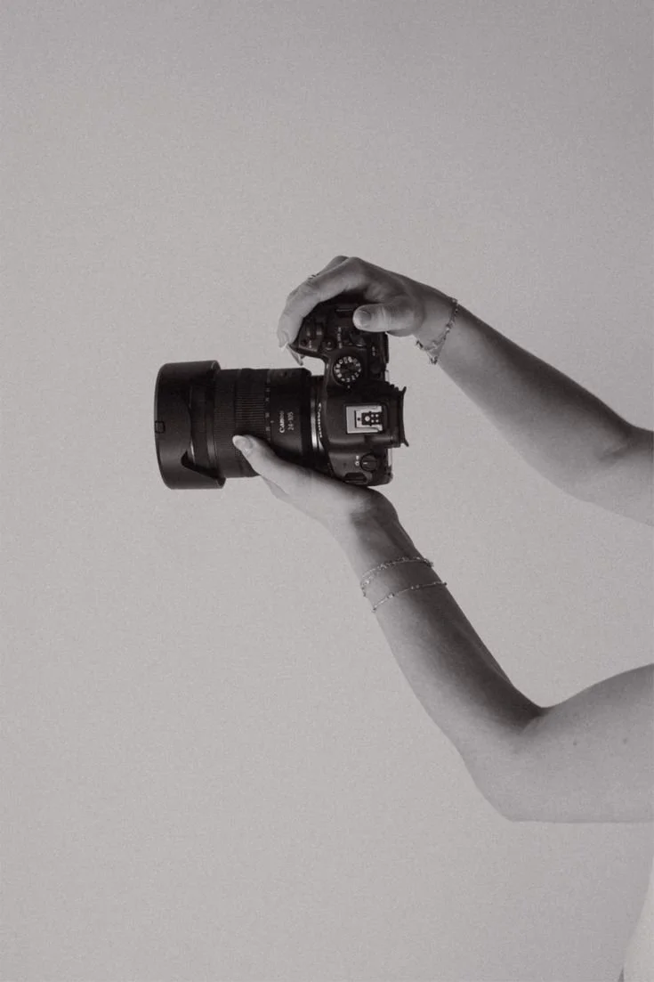 Person holding a DSLR camera against a plain background.