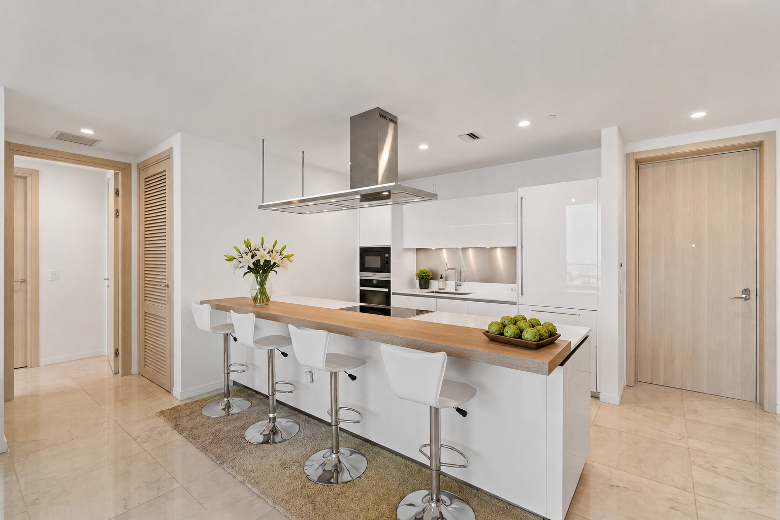Modern kitchen with white cabinets, a wooden countertop island, four white bar stools, a stainless steel range hood, and a vase of white lilies.