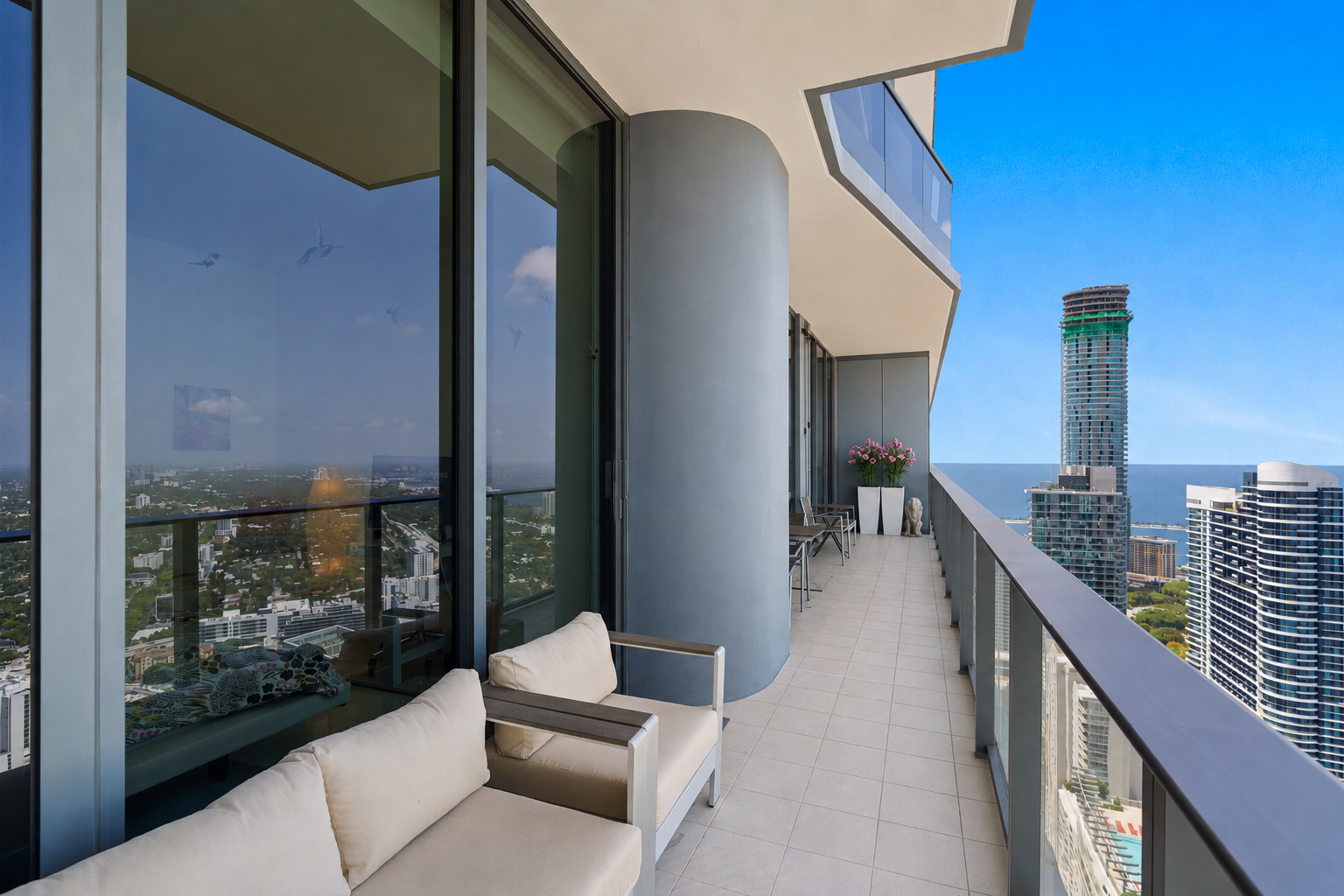 Balcony with seating, potted flowers, and city skyline view of tall buildings and ocean
