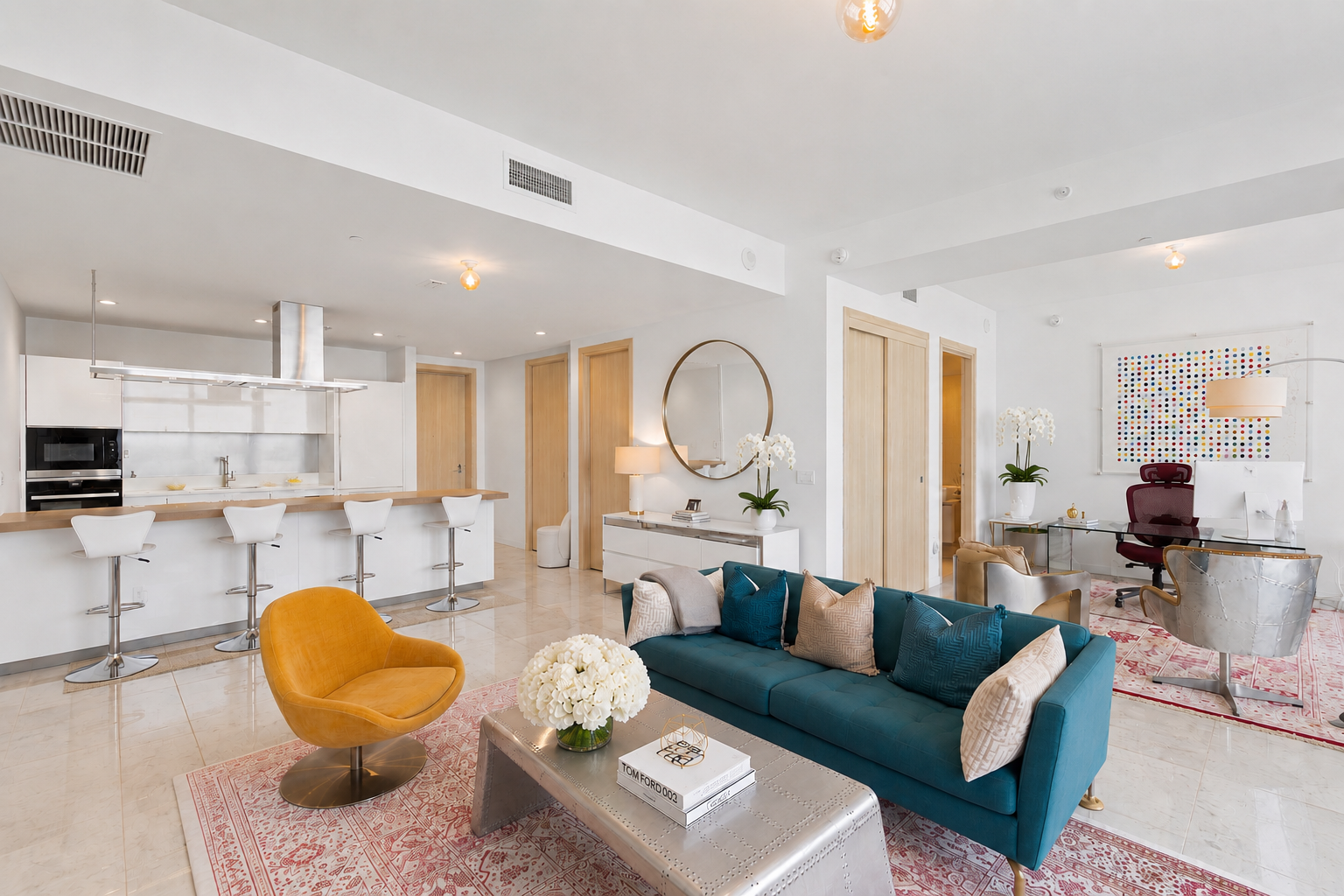 Open-concept living space with a kitchen, sitting area, and workspace. White walls, modern furniture, and colorful decor accents.