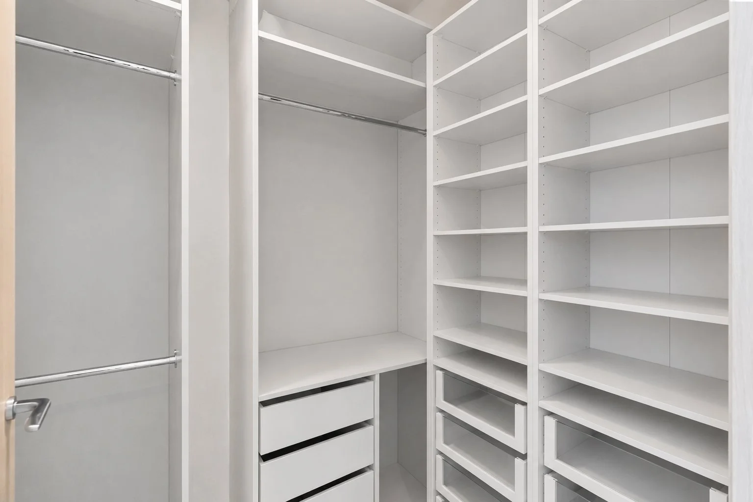 Empty white walk-in closet with shelves, drawers, and hanging space.