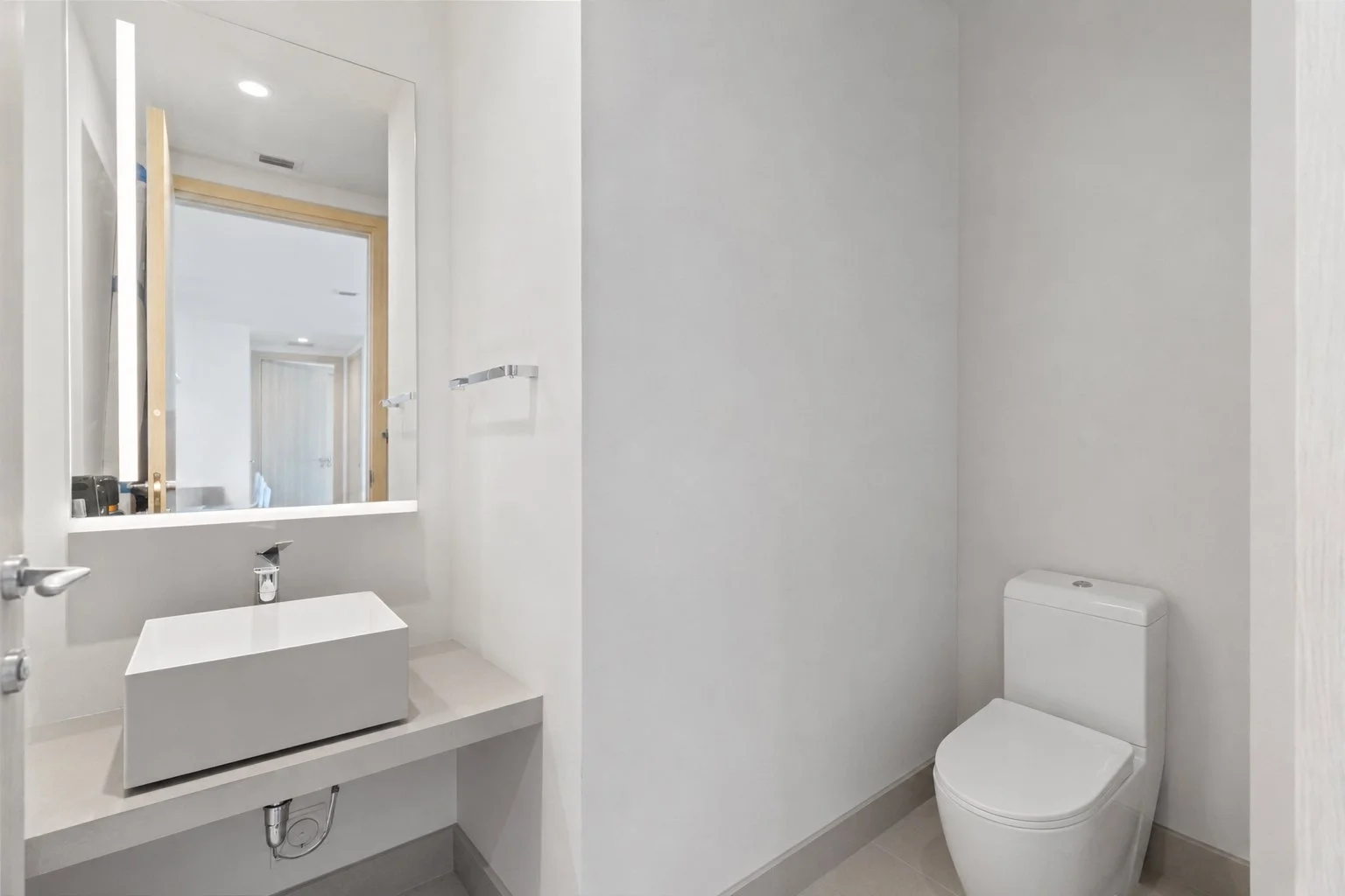 Modern bathroom with a white toilet and a white rectangular sink with a large mirror above it, all in minimalistic decor.
