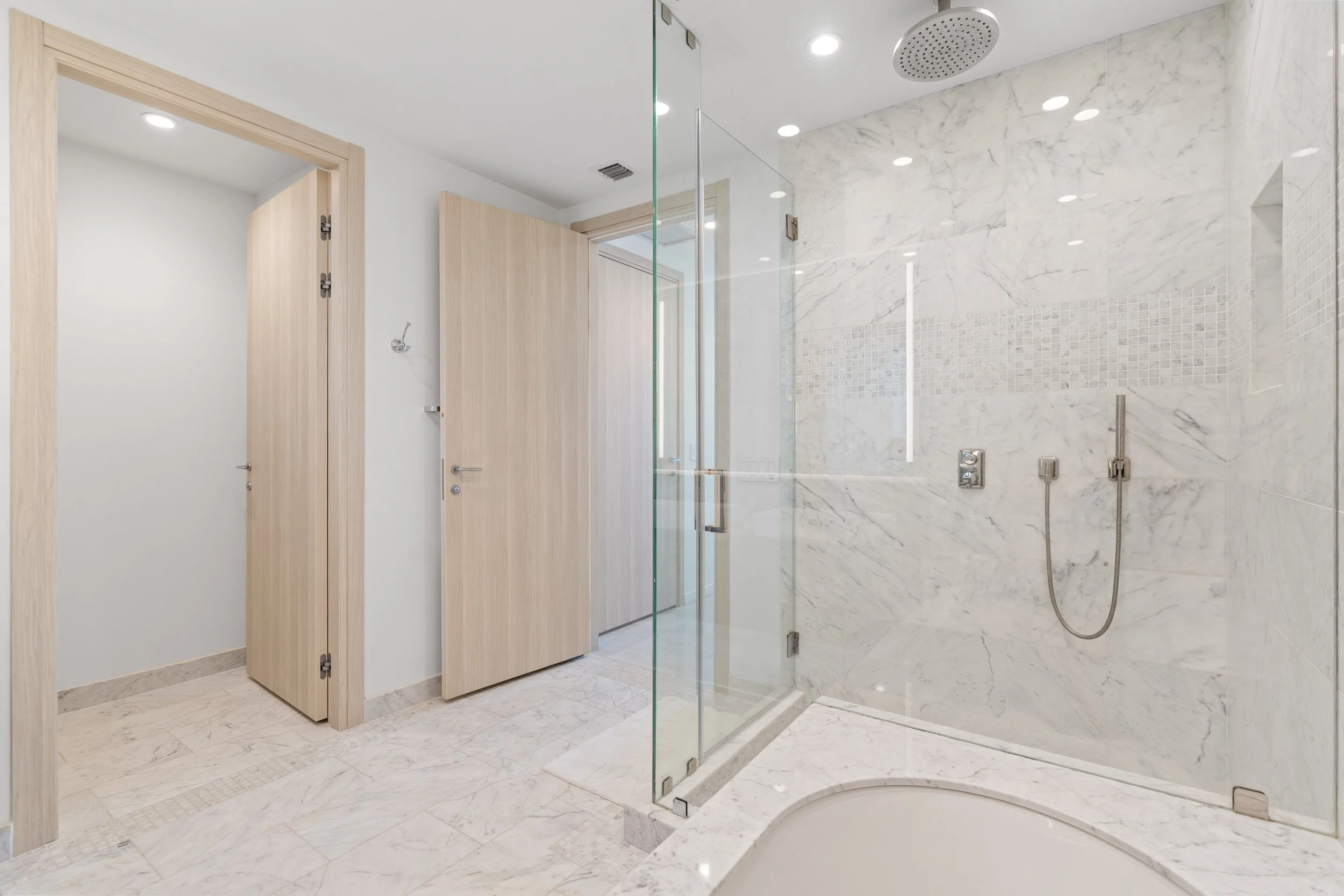 Modern bathroom with marble tiles, a glass shower enclosure, rain showerhead, and wooden doors for the lockers or cabinets.