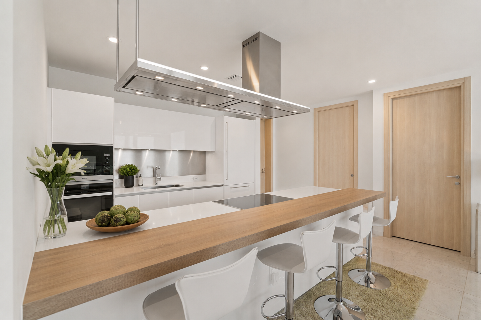 Modern kitchen with white cabinetry, a wooden breakfast bar, bar stools, and stainless steel appliances.