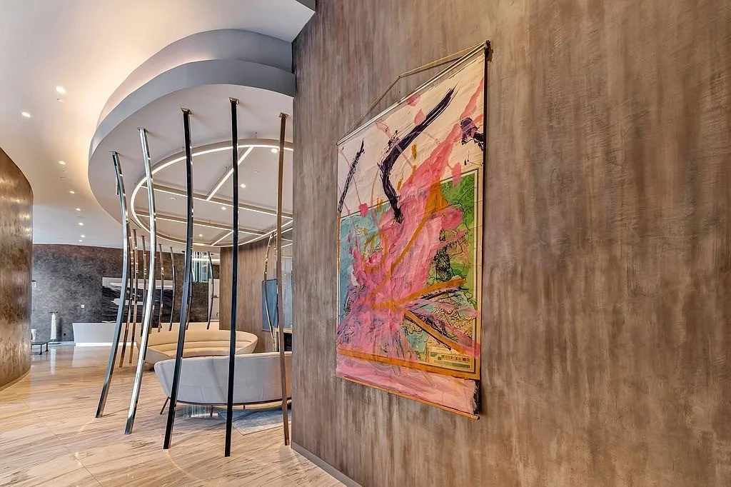 Modern hotel lobby with curved ceiling, beige seating, and abstract colorful artwork on a textured wall.