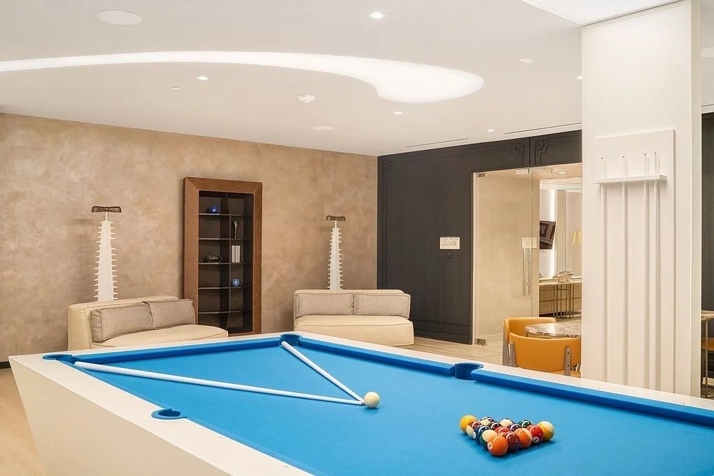 Indoor recreational room with a pool table, two beige sofas, a black bookshelf, and a dark wall with a doorway.