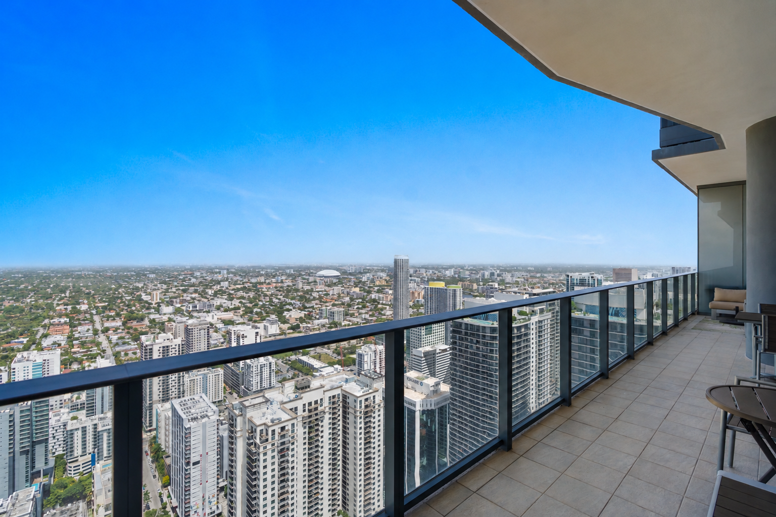 Empty balcony with glass railing overlooking a city skyline with tall buildings and a clear blue sky.
