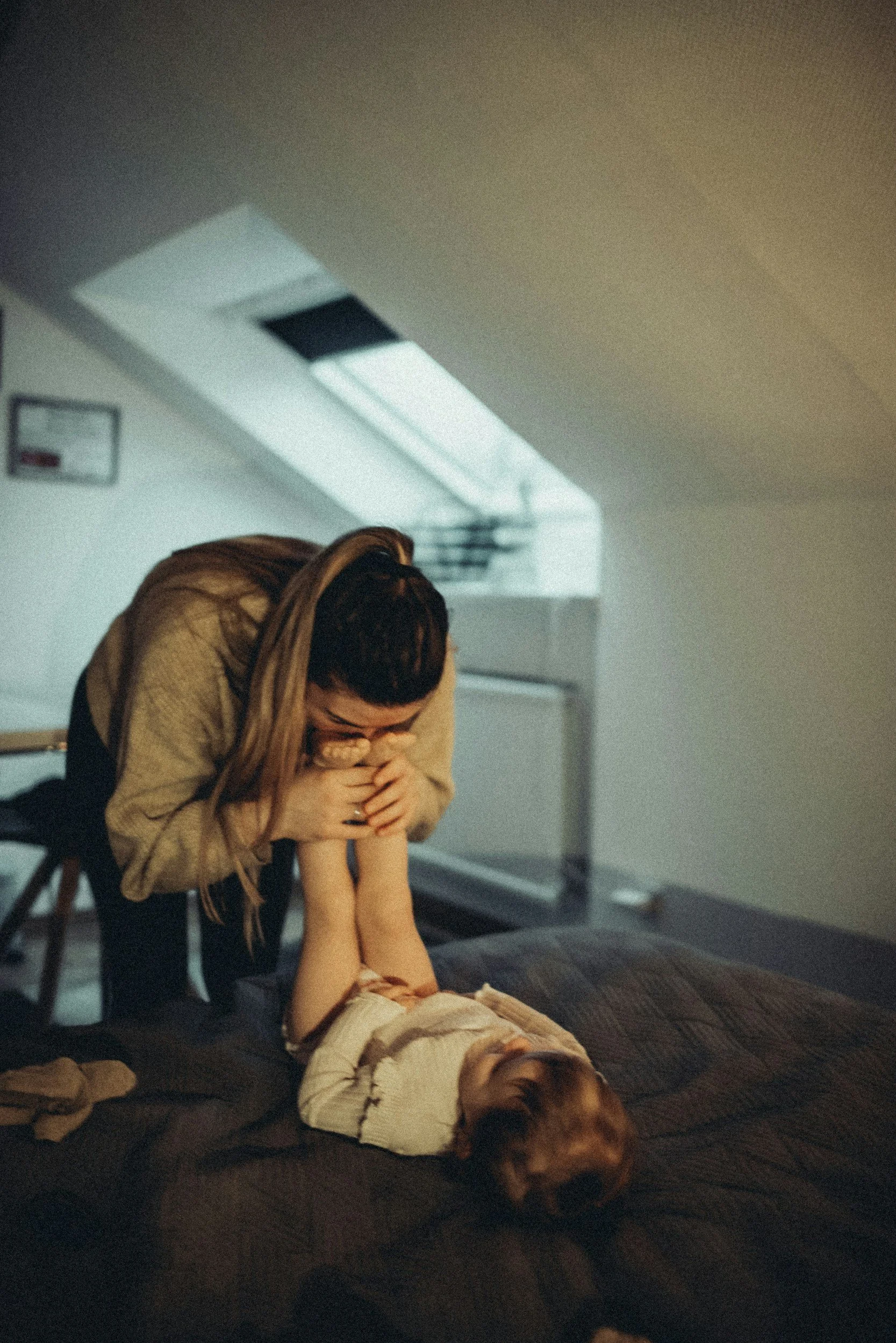Mother playfully holding her child's feet while the child lies on the bed laughing