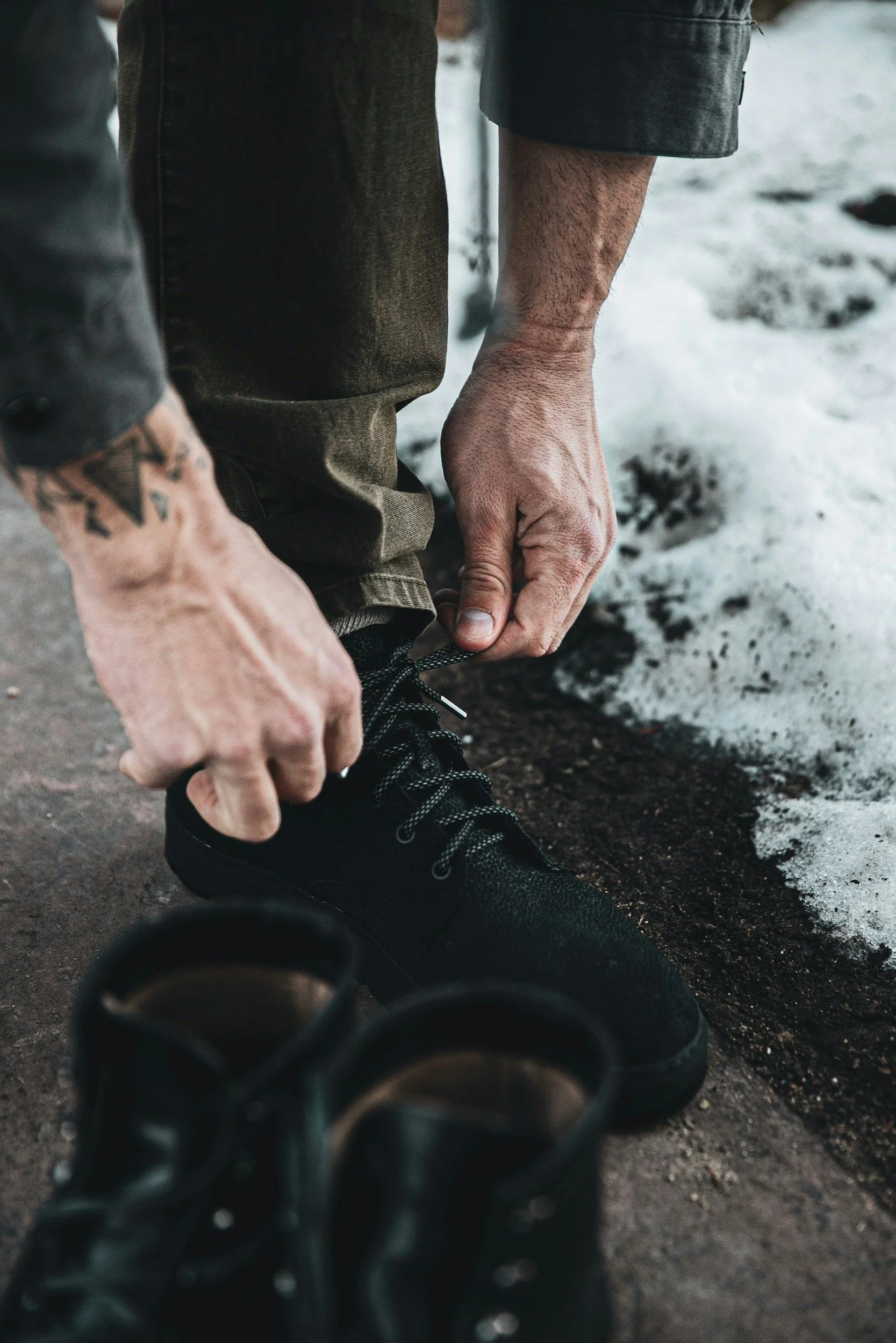 Close-up of a man tying his boot on snowy ground