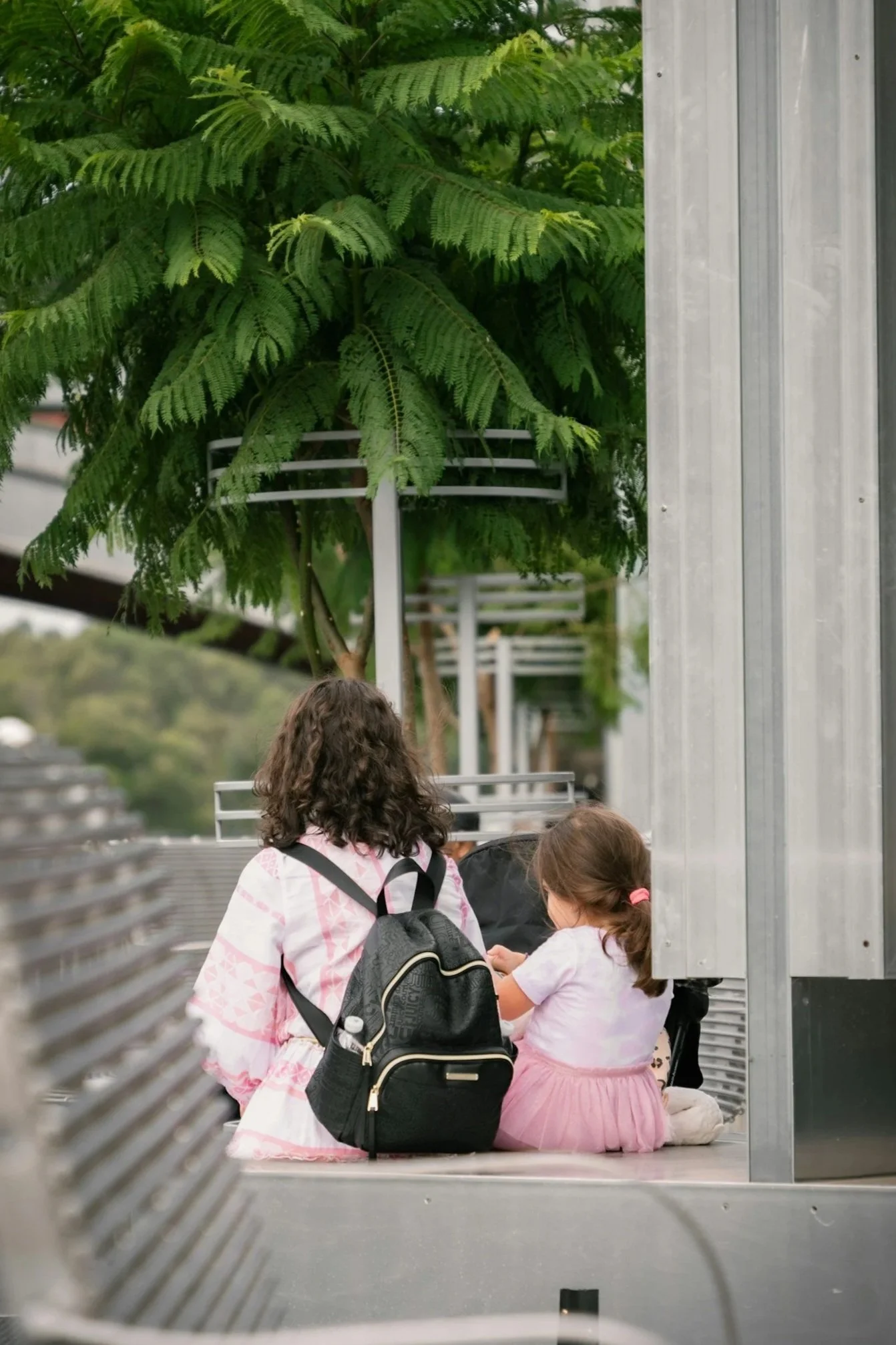 Mother and daughter sitting together on an outdoor bench, seen from behind