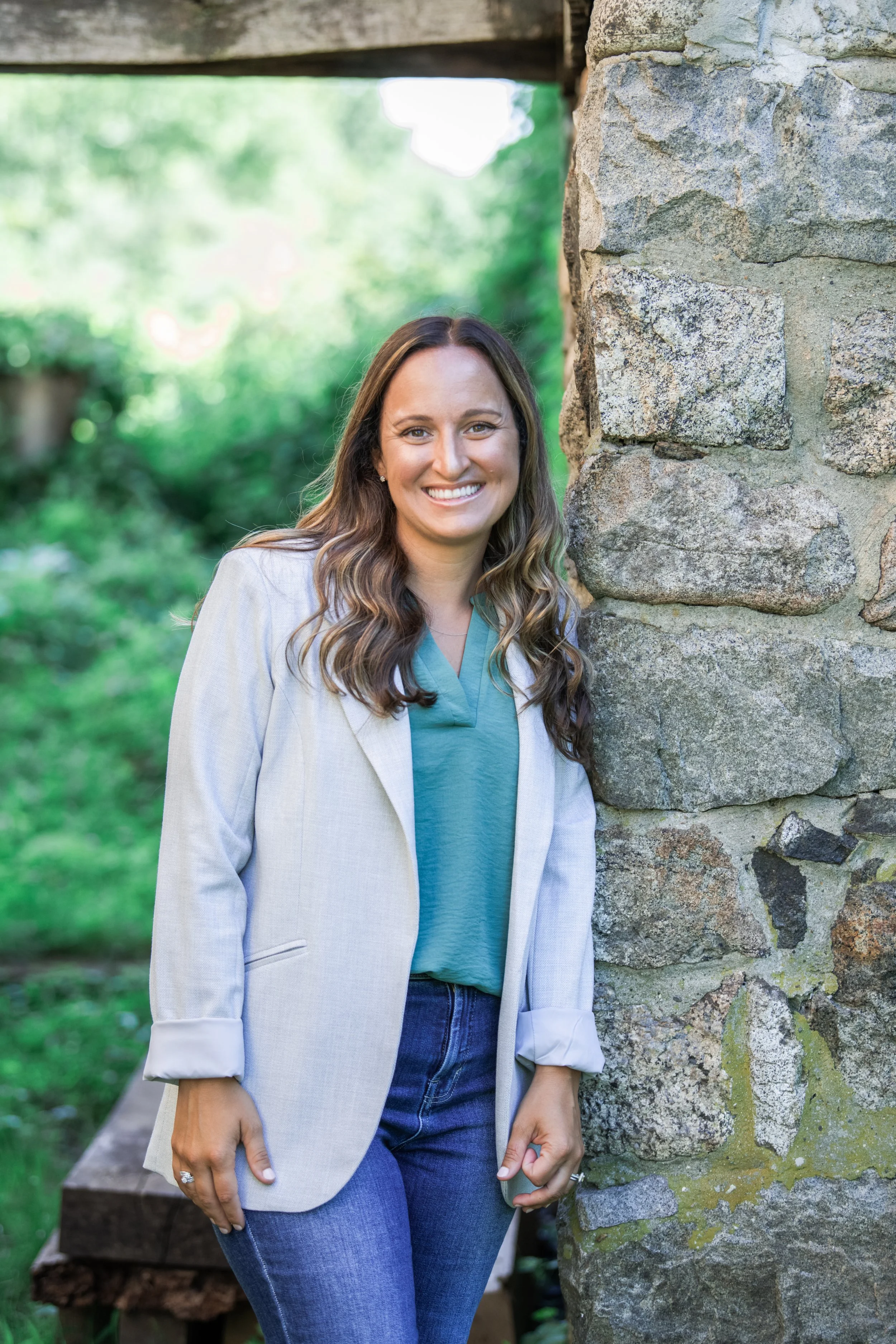 Melissa Parrish, LPC, leaning against a stone wall and smiling, green background