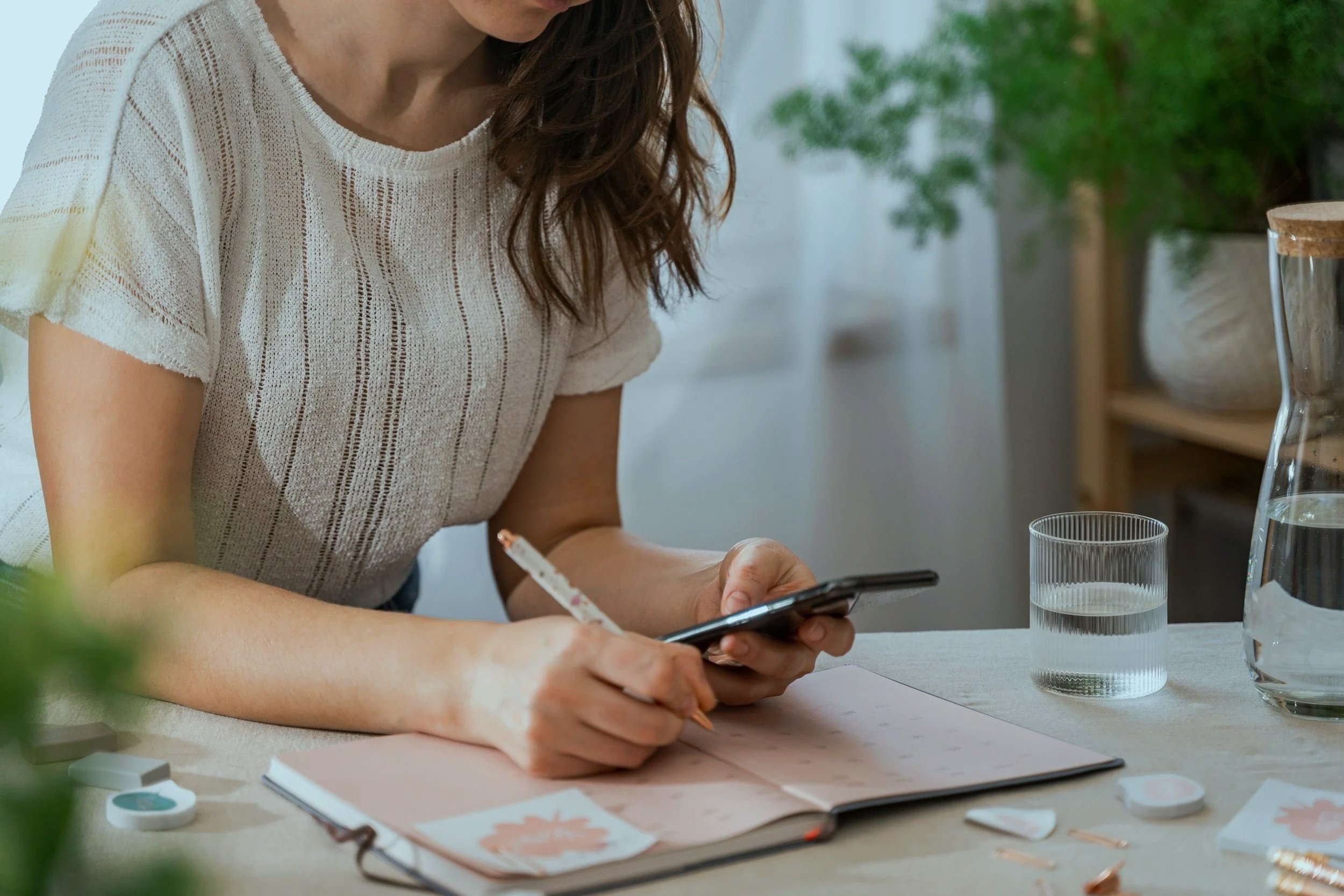 Woman leaning over a planner, holding a pen and phone, managing a busy schedule