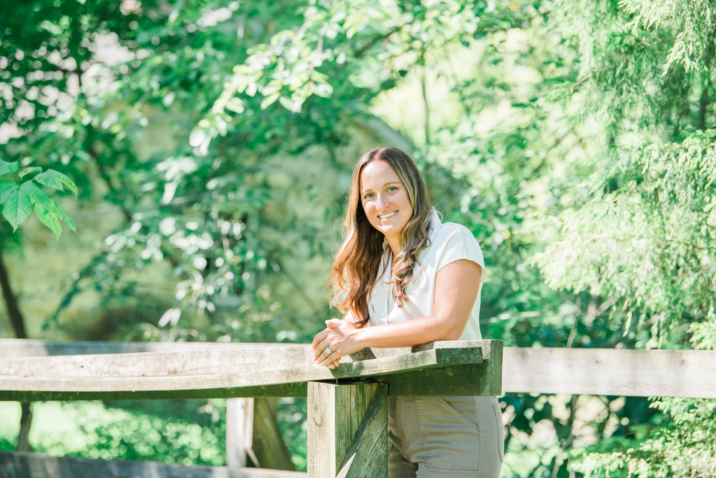 Melissa Parrish, LPC, leaning on a wooden bridge railing and smiling, surrounded by green trees