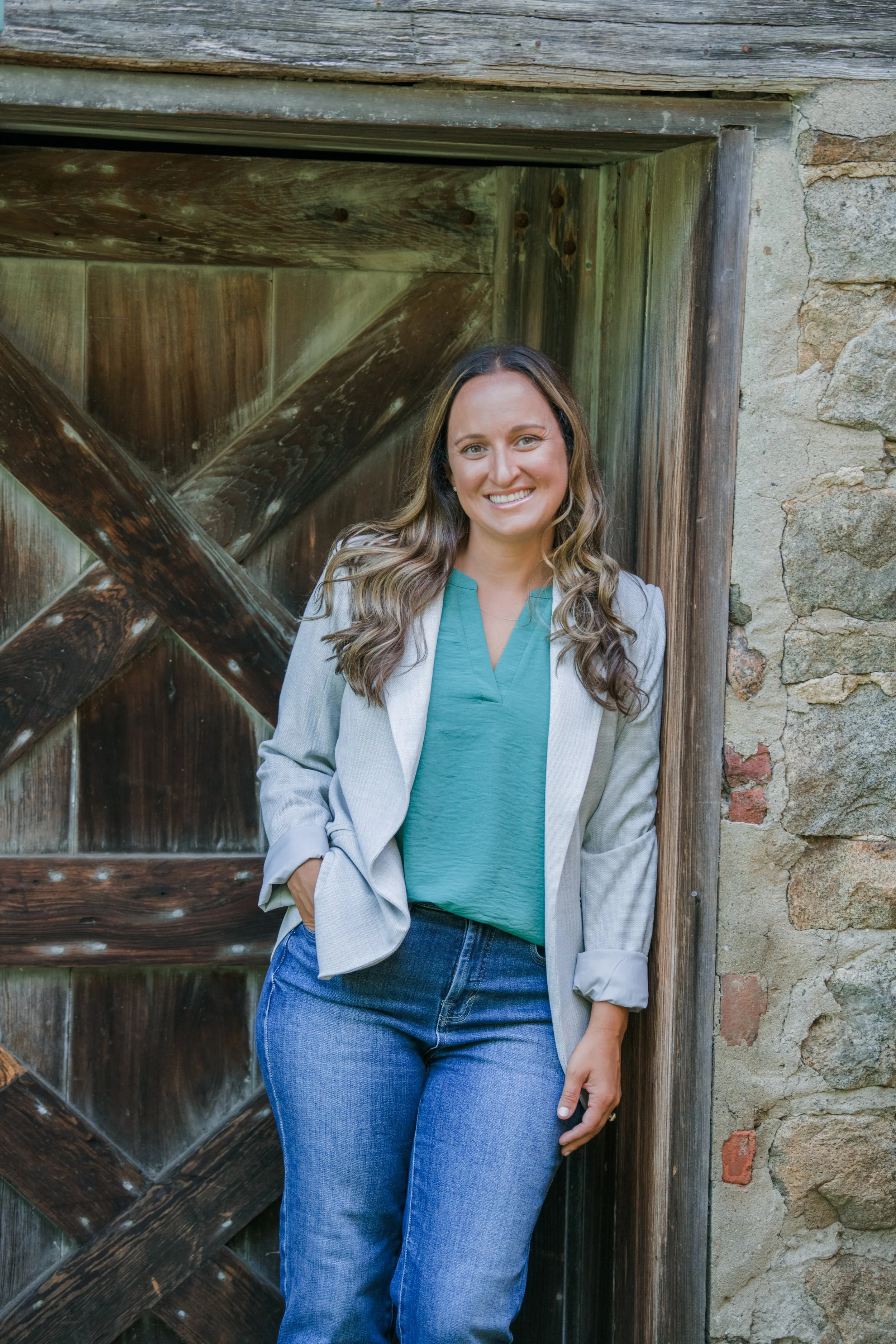 Melissa Parrish, LPC, standing by a wooden door and stone building, smiling at the camera