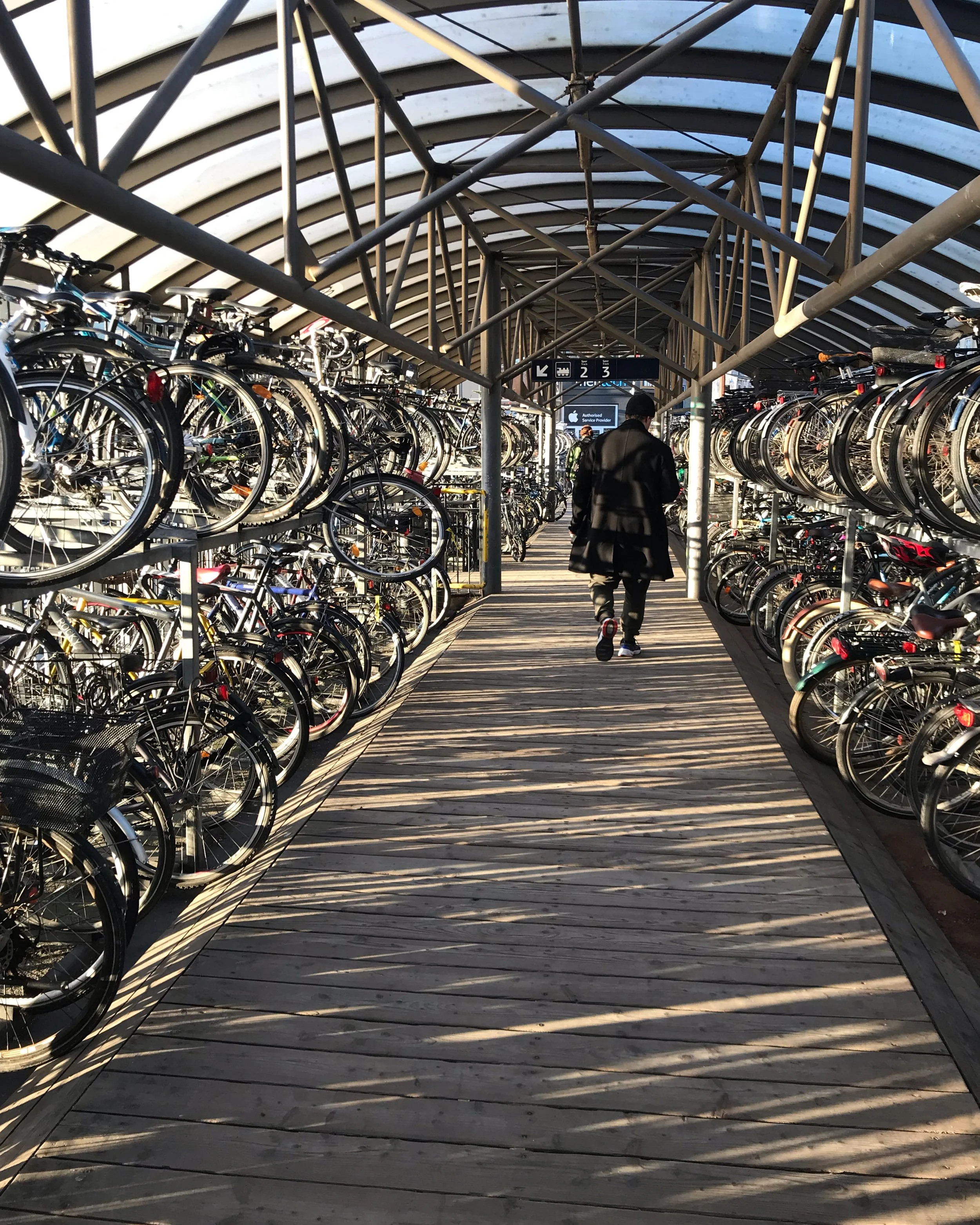 Cykler parkeret under et skur med bueformet tag, en person går gennem området.