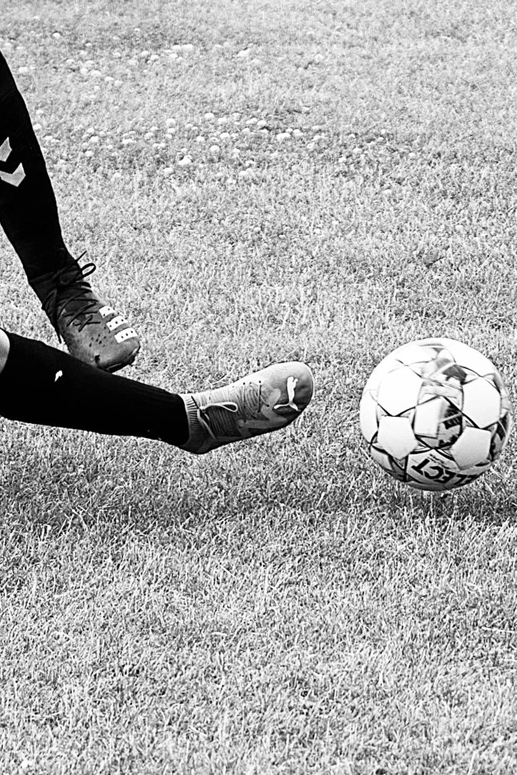 En fodbold, der bliver sparket af en spiller på en græsplæne.