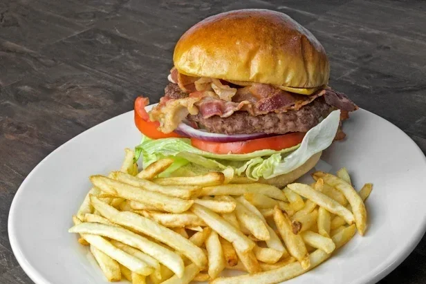 A plate with a cheeseburger featuring bacon, lettuce, tomato, and a bun, accompanied by a side of French fries.