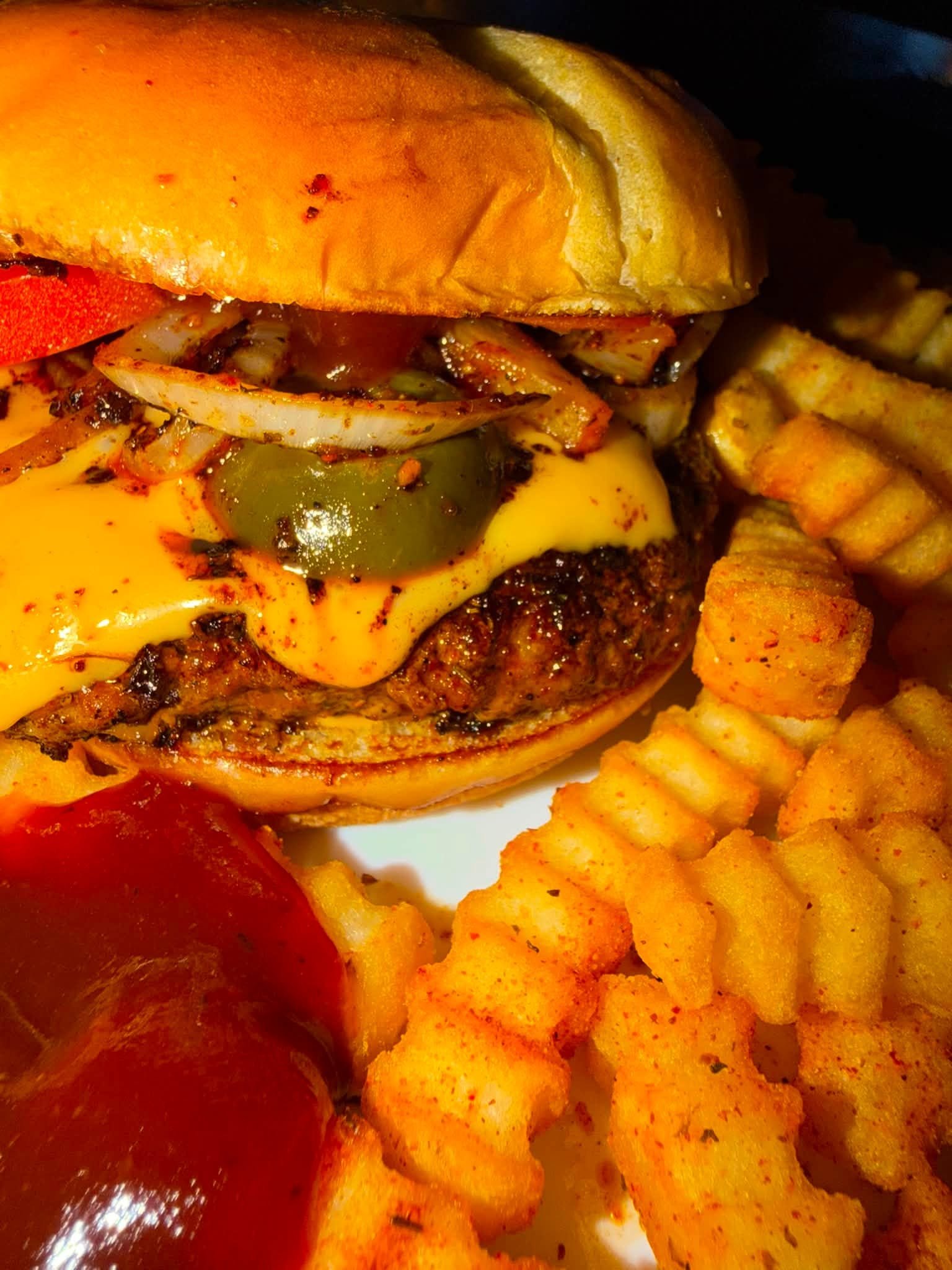 Close-up of a cheeseburger with grilled onions, pickles, and ketchup, accompanied by crinkle-cut fries.
