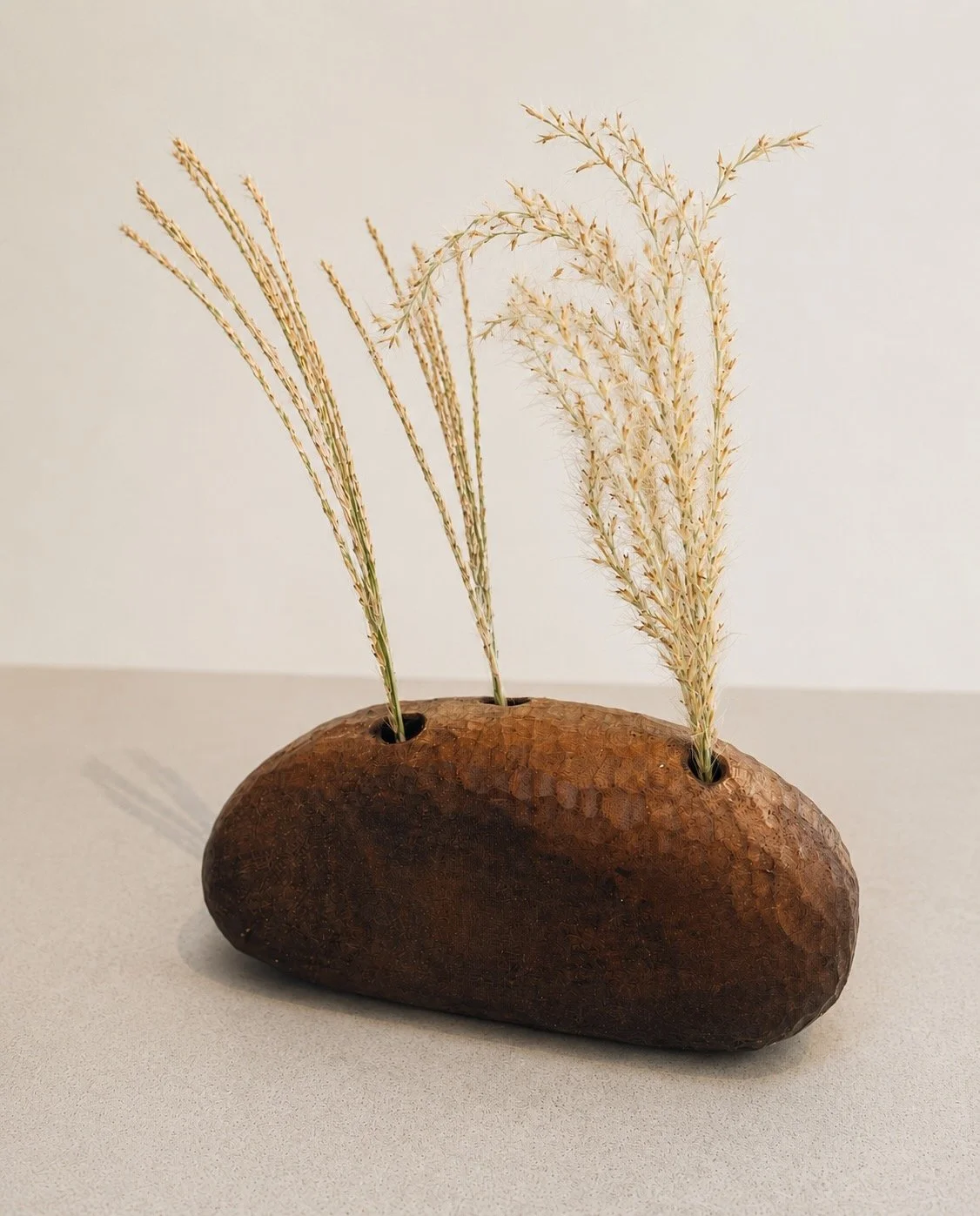 Low hand-carved wooden vessel holding dried grasses