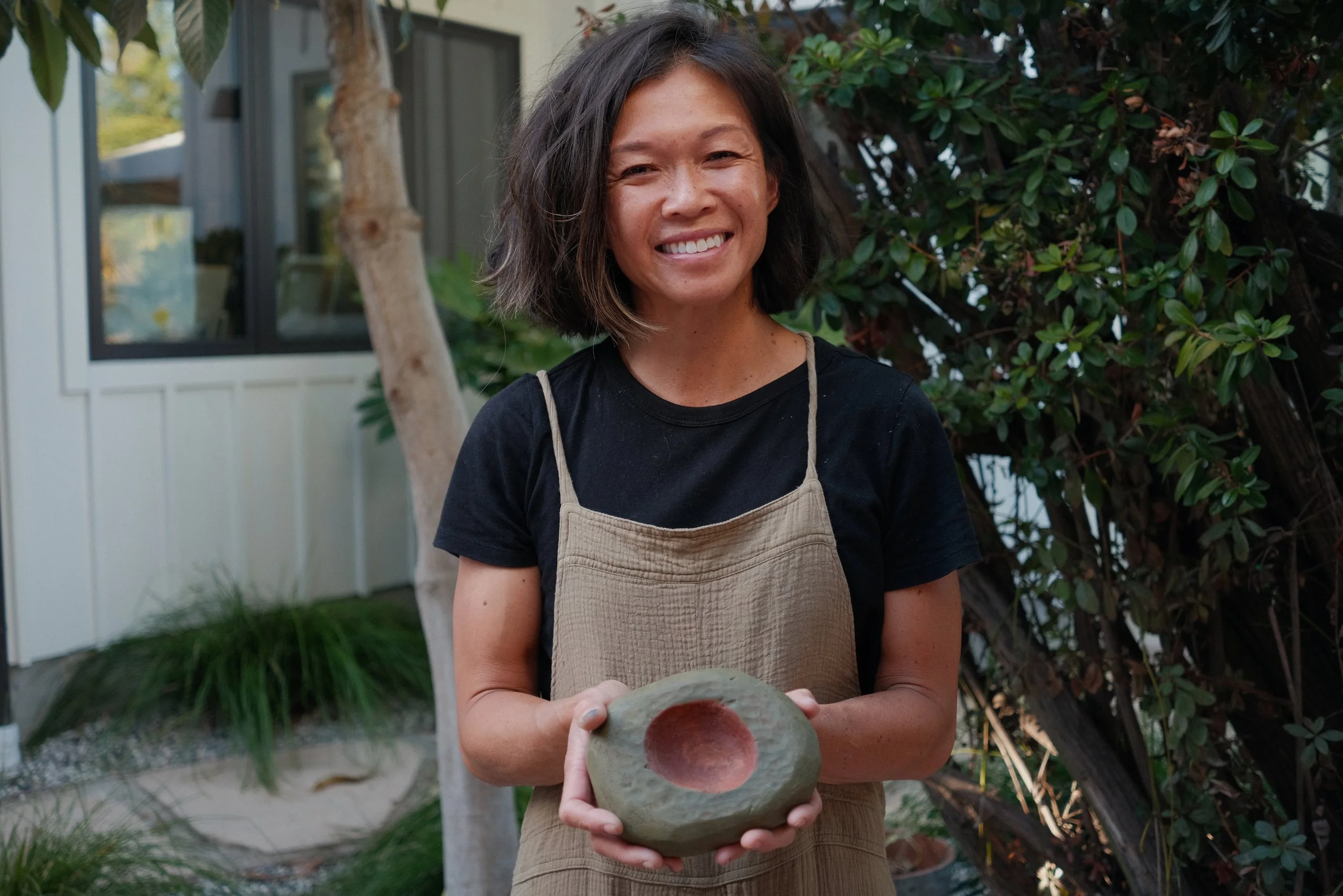 Caroline Tien standing outdoors in Santa Cruz holding a hand-carved wooden sculpture