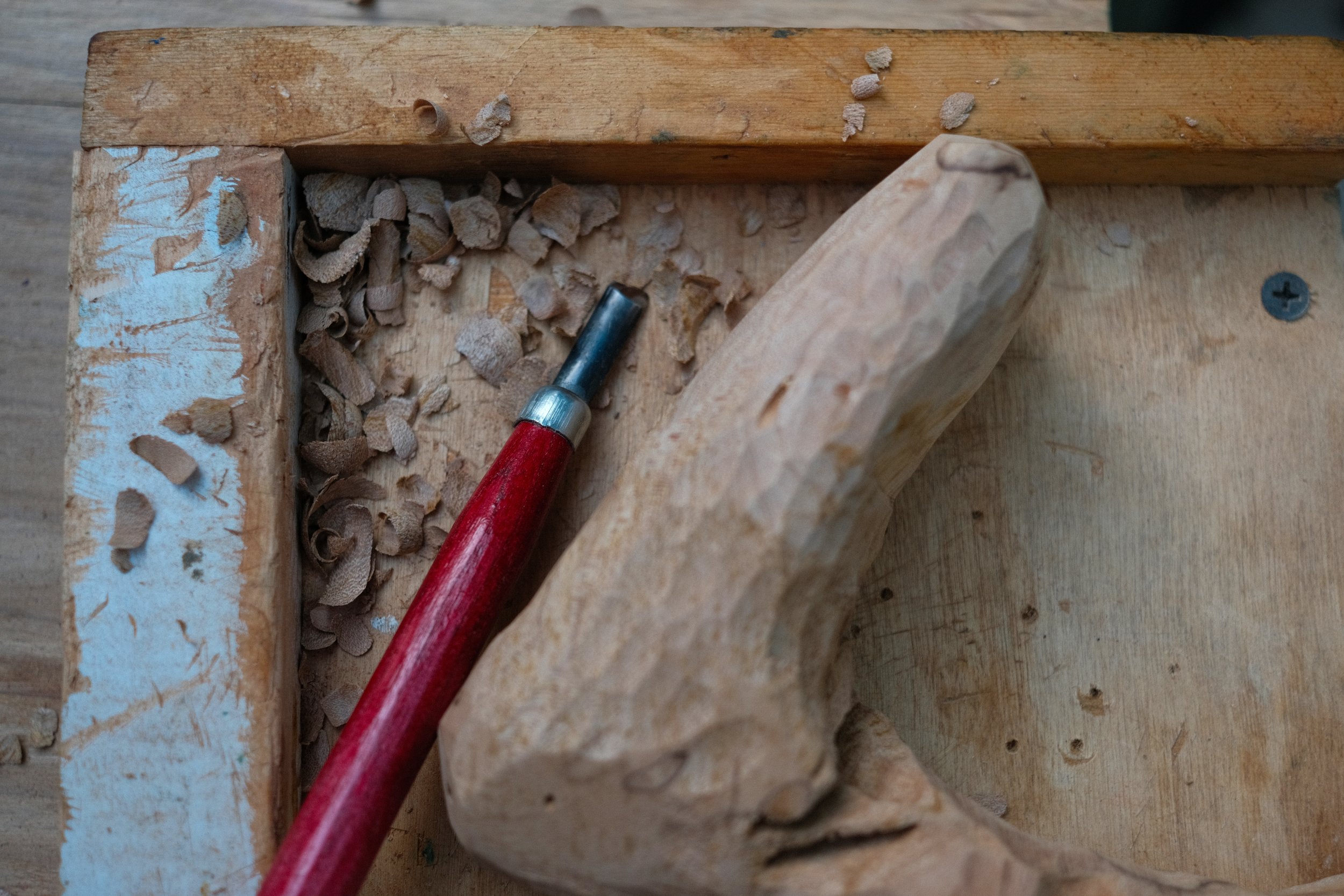 Hand-carved wood form in progress with carving tool and wood shavings