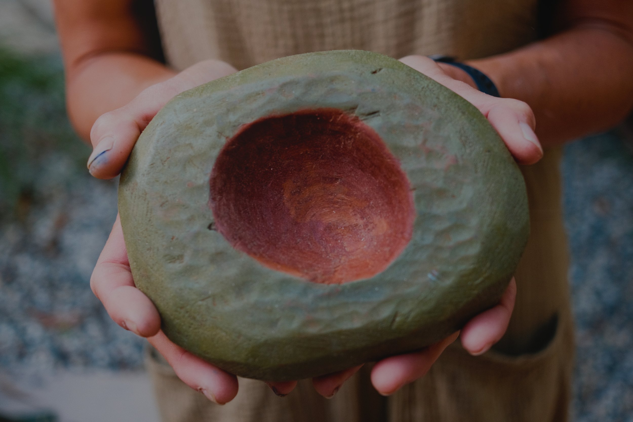 Hand-carved wooden bowl held in two hands. Exterior painted moss green with oil paints