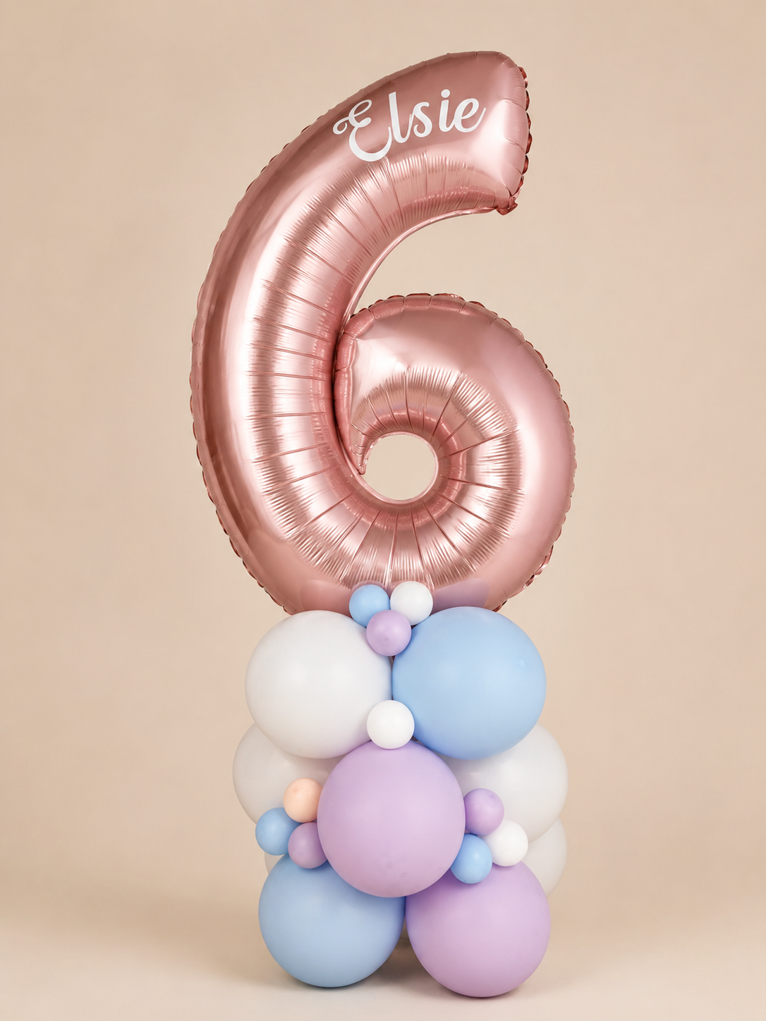 Personalised rose gold number 6 balloon with name Elsie, stacked on pastel blue, lilac and white latex balloons for a 6th birthday display.