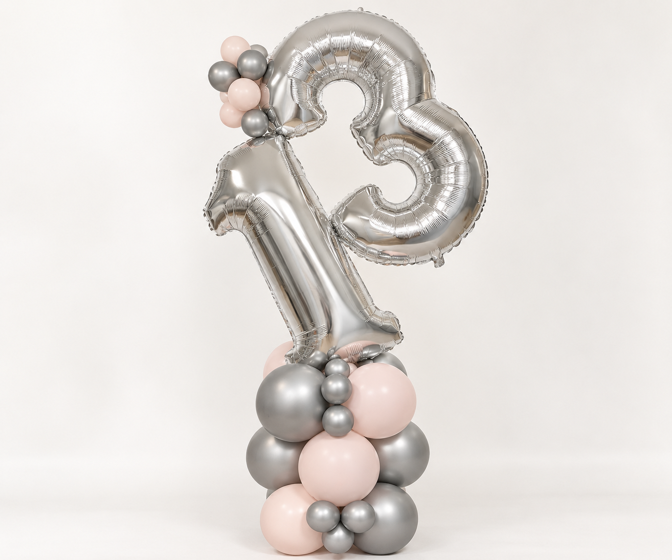 Silver number 13 balloon stack tilted at an angle, standing on chrome silver and blush pink latex balloons for a 13th birthday display.