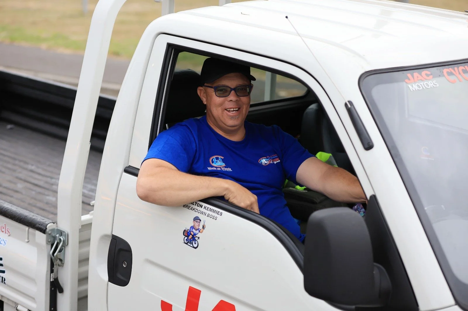A man wearing glasses and a blue T-shirt sitting in a white utility truck, smiling at the camera.