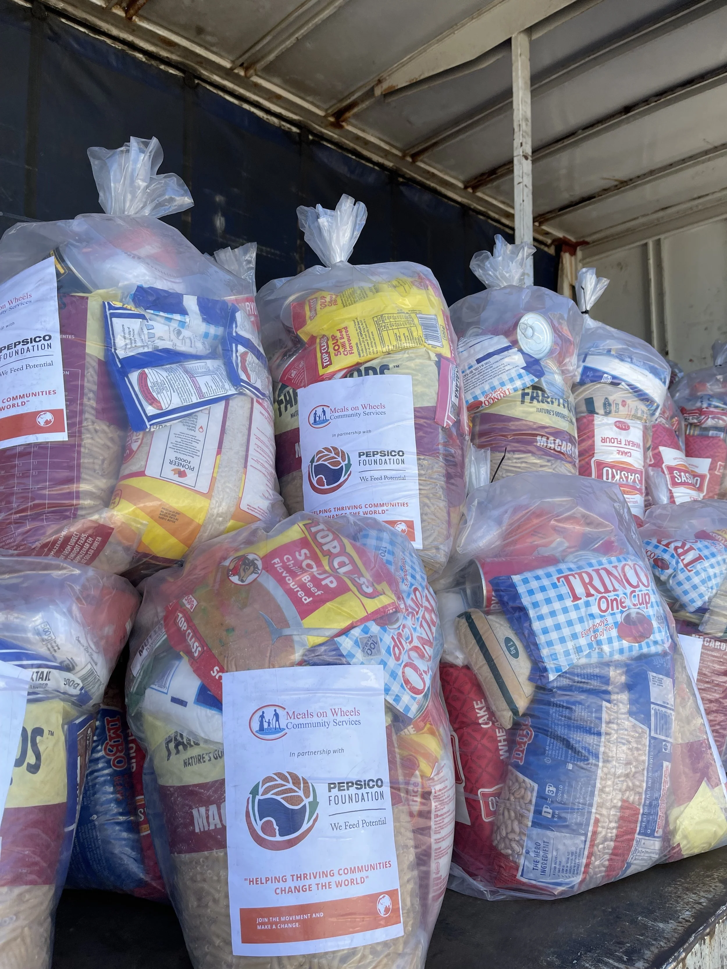 Bags of food donations in clear plastic, labeled with the Meals on Wheels logo and Pepsico Foundation logo, on a truck. Emergency Food Parcel Delivery with Donor Pepsico Foundation