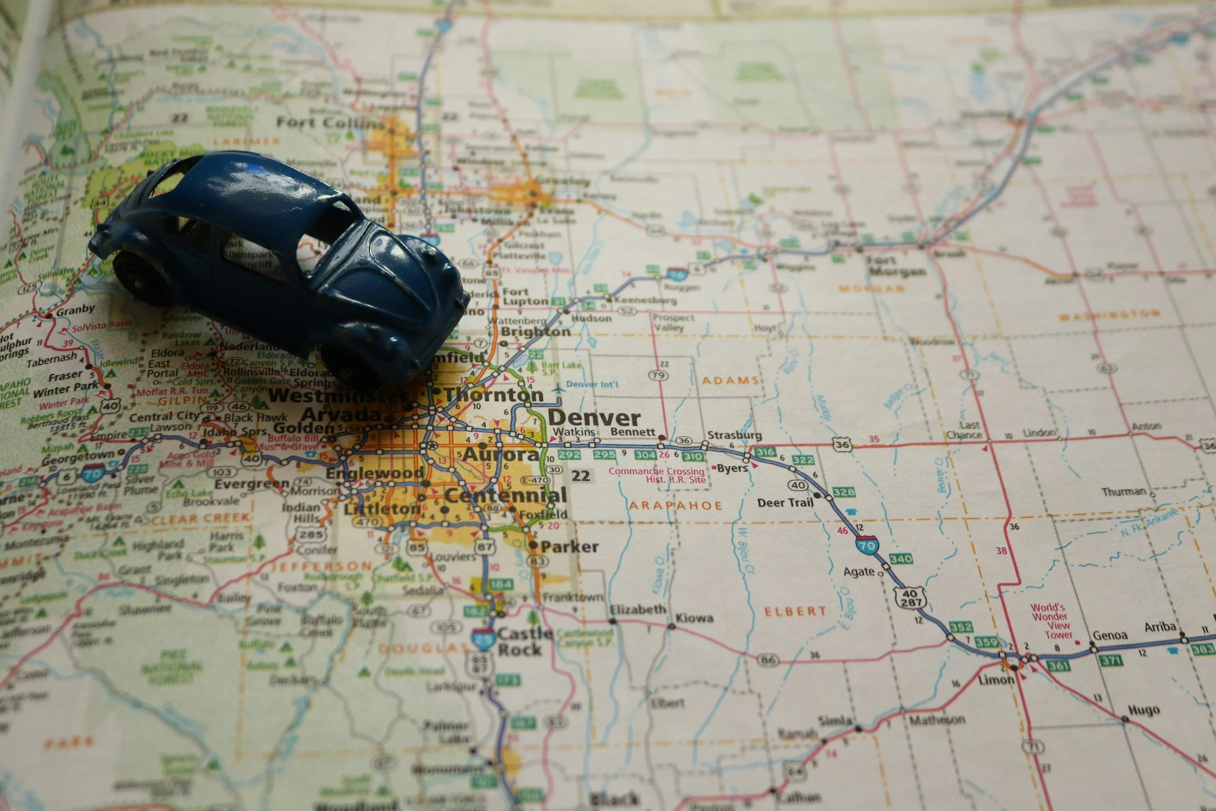 A small blue toy car placed on a detailed map of Colorado, showing cities like Denver and Colorado Springs.
